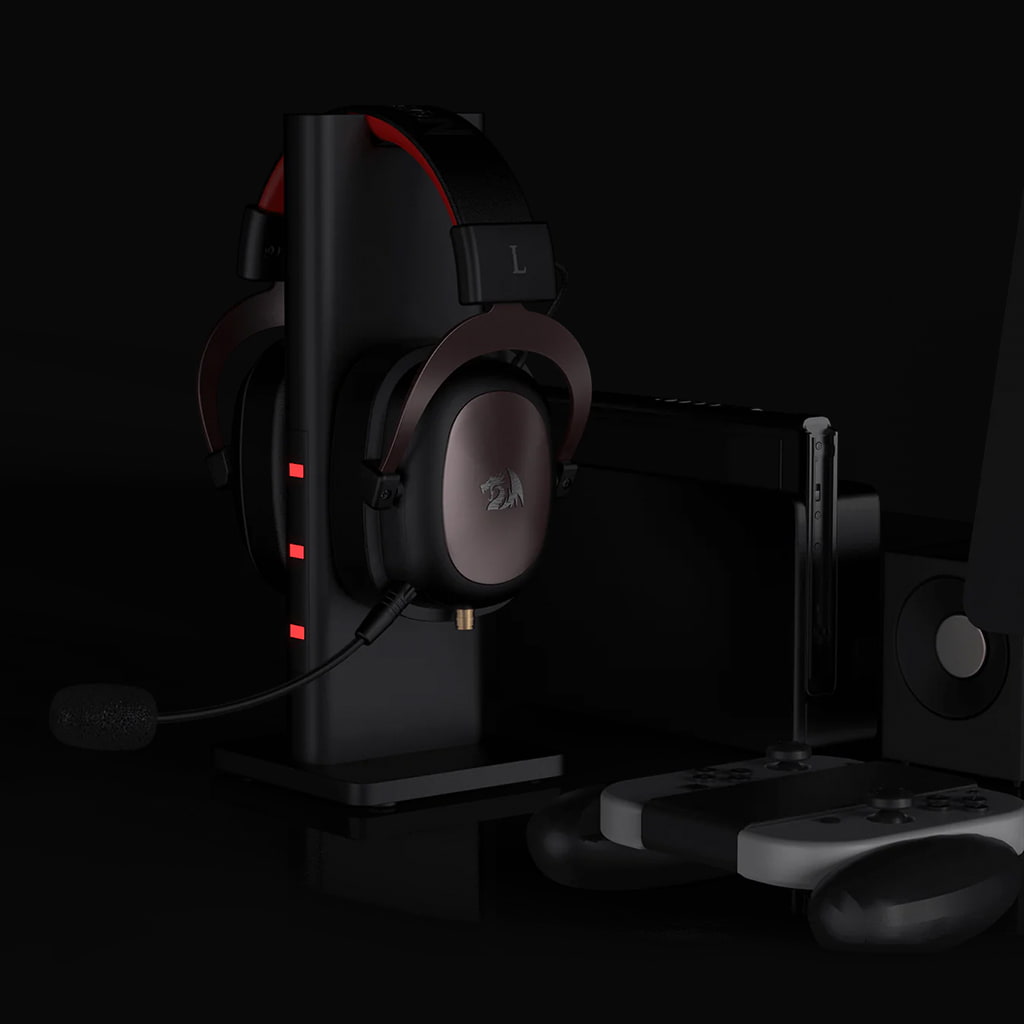 Redragon H510 Zeus gaming headset on a stand in a gaming setup with controller and phone