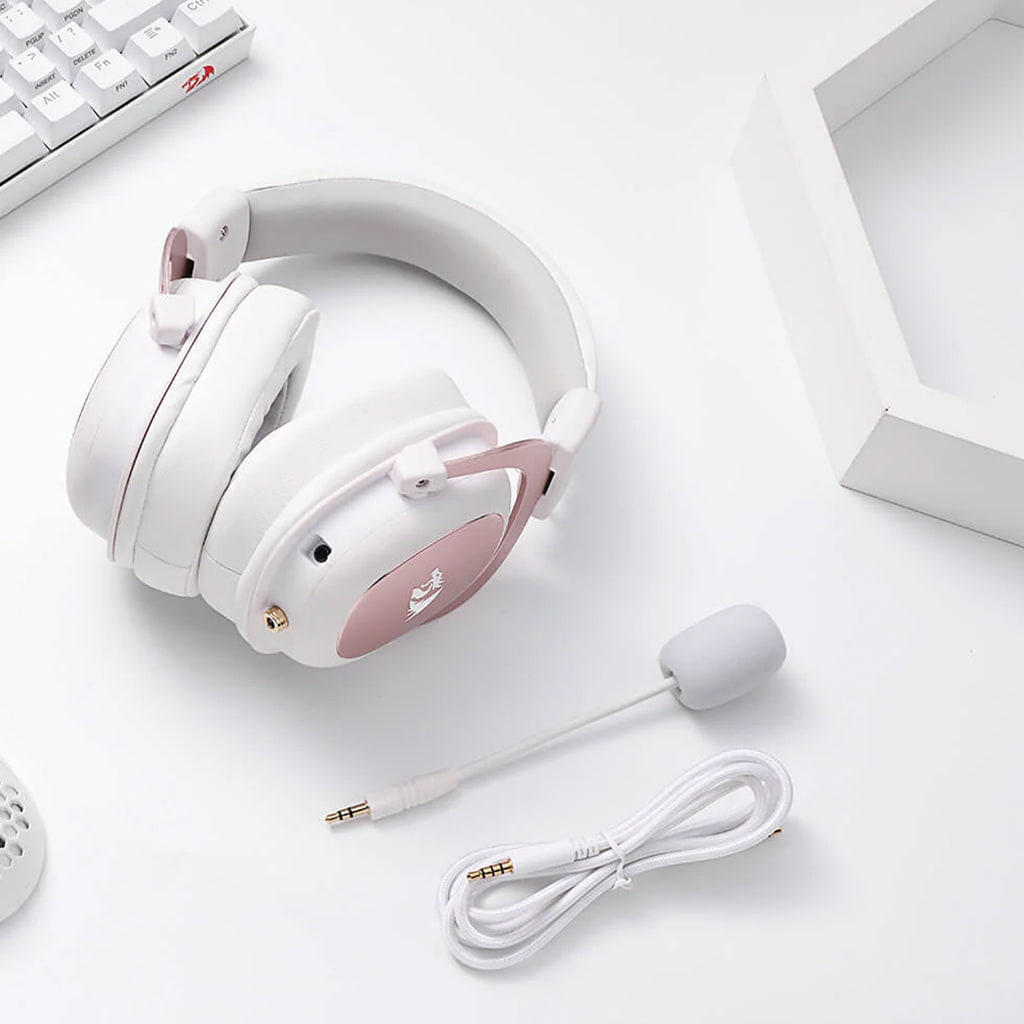 White Redragon H510 Zeus gaming headset with detached microphone and cable, arranged on a white surface alongside a keyboard